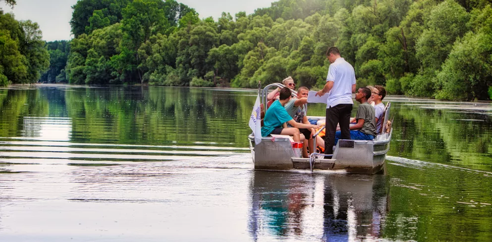 Eine Gruppe Jugendlicher bekommt in einem Nachen sitzend Erklärungen zur Natur durch den Bootsführer